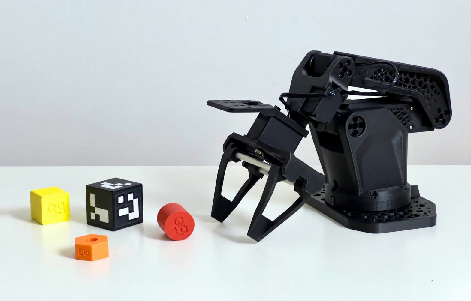 Собранная рука-исполнитель SO-ARM102 из чёрного PET-CF с параллельным захватом рядом с цветными учебными кубиками и цилиндром